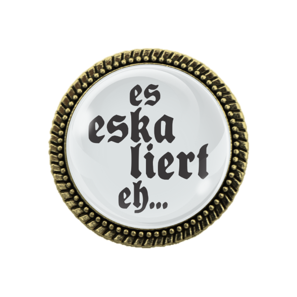 Detailaufnahme der Trachtenbrosche „Es eskaliert eh!“ in Bronze auf einer Lederhosn