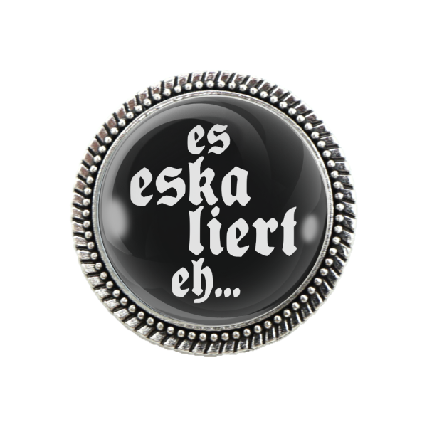 Trachtenbrosche in Silber mit schwarzem Hintergrund und weißem Spruch „Es eskaliert eh!“